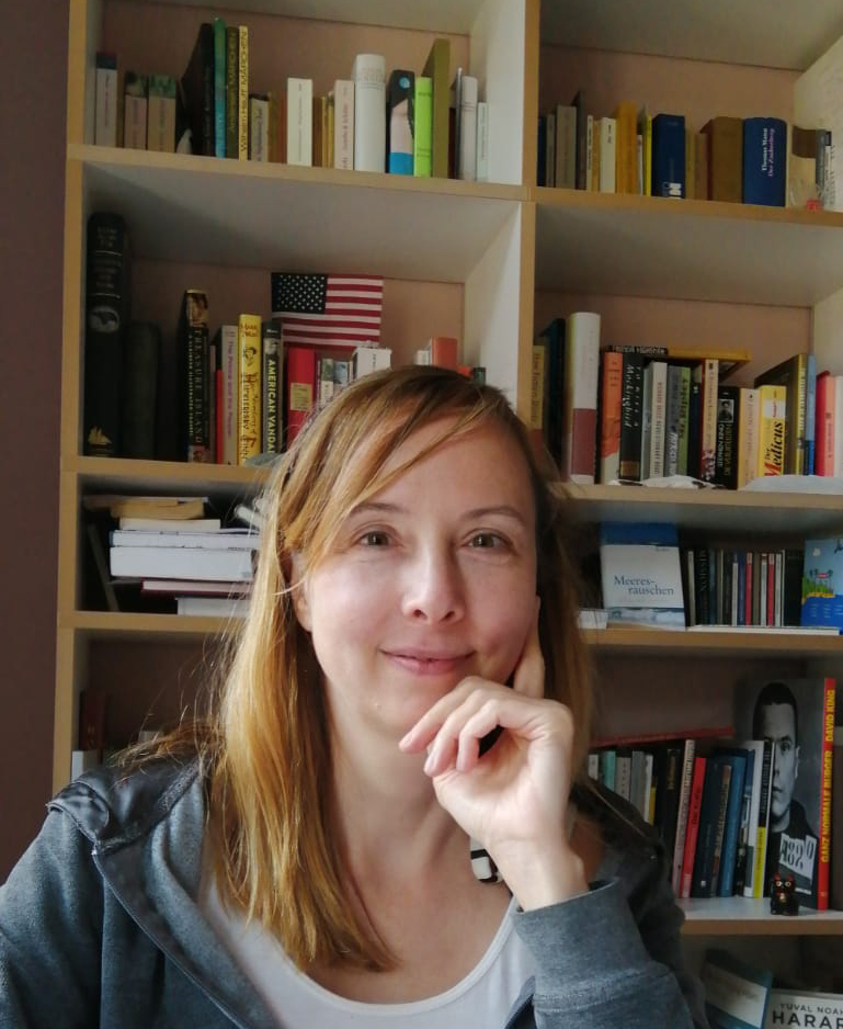 Diana Feuerbach sitzt vor ihm Bücherregal